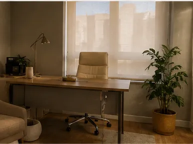 Consultório preparado para atendimento psicológico, com luz natural, madeira e plantas.